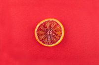 Schijfje bloedsinaasappel tegen rode achtergrond.