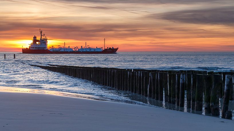 Vrachtschip vaart voorbij aan de kust van Zeeland tijdens zonsondergang van Menno Schaefer