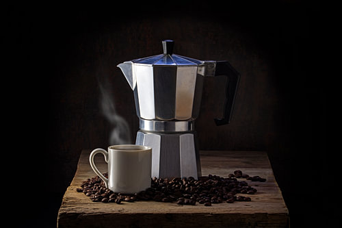 Italienische Kaffeemaschine, Tasse dampfender Kaffee und ganze Kaffeebohnen auf einem alten rustikal