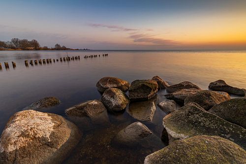 Gouden zonsopkomst aan het IJsselmeer met stenen en een golfbreker van houten paaltjes