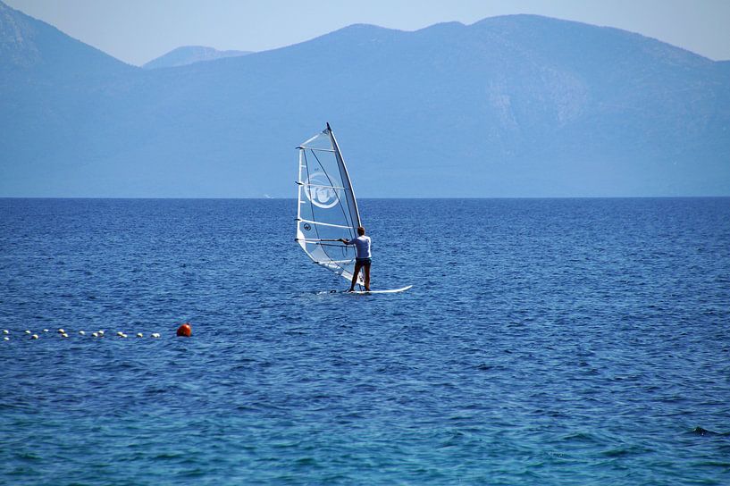 windsurfer wit met doorzichtig zeil surfend in het blauw landschap van wil spijker