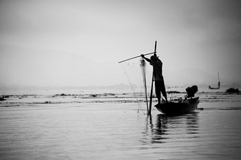 Silhouet van een visser met zijn visnet op het Indiemeer in Myanmar