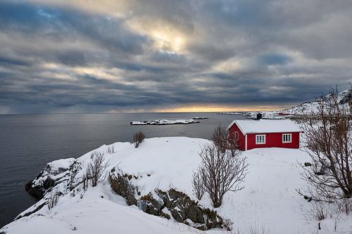 red hut in winter landscape in front of the sea at sunset with clouds