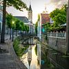Church tower in Amersfoort behind a canal with people on a terrace by Bart Ros