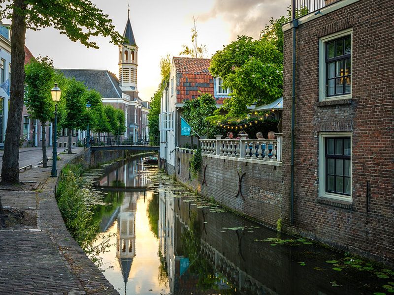 Church tower in Amersfoort behind a canal with people on a terrace by Bart Ros