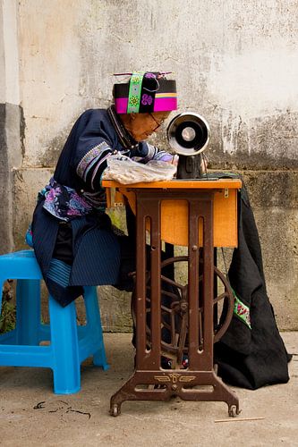 Woman in traditional dress from China sews clothes on the sewing machine