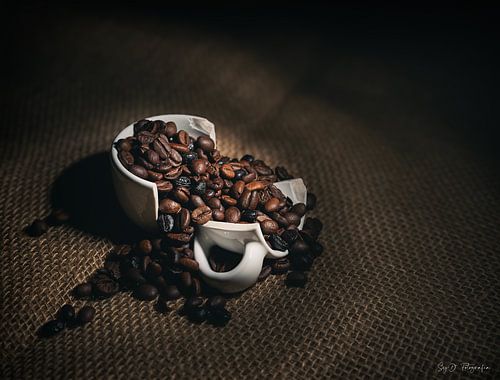"Zerbrochene weiße Kaffeetasse mit gerösteten Bohnen auf Sackleinen in dramatischer Beleuchtung von SyD Fotografia