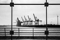 Silhouetten van havenkranen zijn te zien door een raam