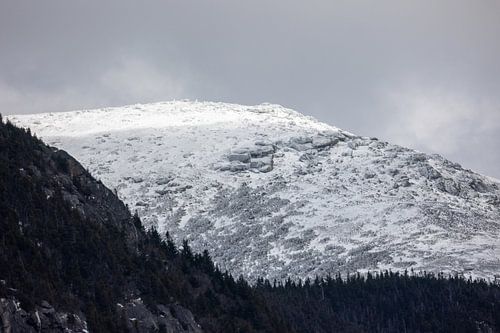 Een majestueuze, met sneeuw bedekte bergtop onder een bewolkte winterhemel, met een bergkam begroeid met naaldbomen en rotsachtig terrein