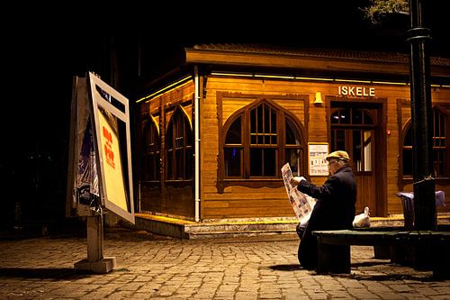 Man leest zijn krant op een bankje, in de avond in Istanbul.