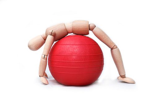 Modellpuppe aus Holz macht eine Übung auf einem Gymnastikball