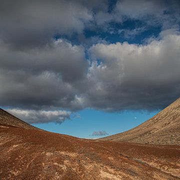 Een zware wolkenlucht en een klein dal tussen twee heuvels.