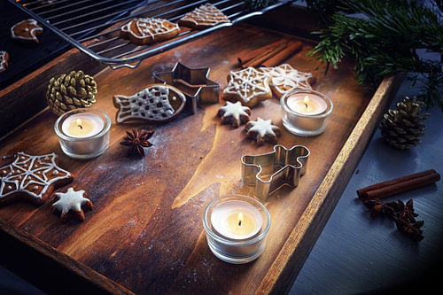 Brennende Kerzen, Lebkuchen- und Keksausstecher auf dunklem Holztablett, weihnachtliches Arrangement