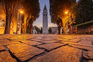 Die Basilika von Aquileia am Ende einer klassischen Kopfsteinpflasterstraße, umgeben von Laternenpfählen und Zypressen
