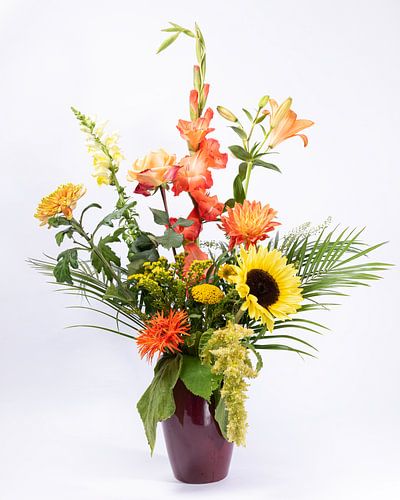 Een boeket met gele en oranje kleurige bloemen in een donker rode vaas