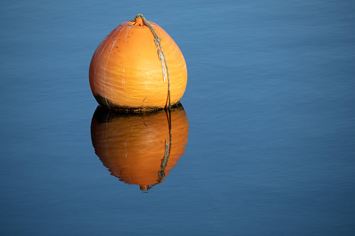 Orangefarbene Boje mit Spiegelung im blauen, ruhigen Wasser eines Sees, Konzept für Entspannung, Pau