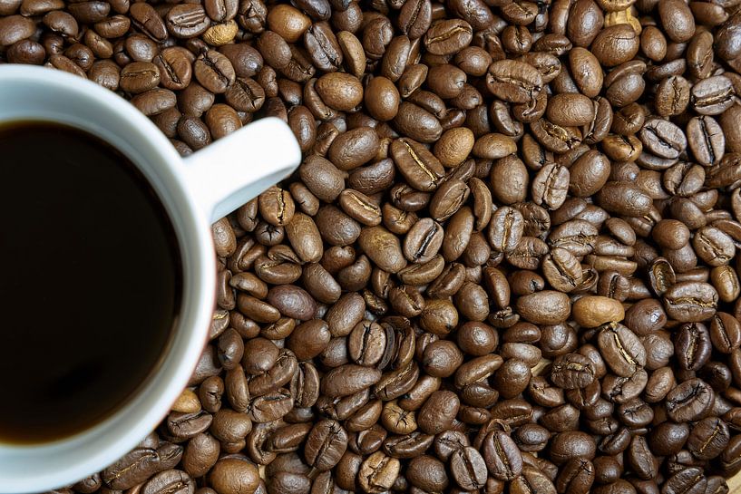 des grains de café fraîchement torréfiés et une tasse de café sur une table de cuisine par Heiko Kueverling