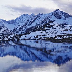 Ein Fischerboot segelt im Spiegelbild der schneebedeckten Berge auf den Lofoten