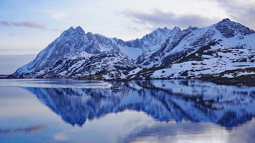 Ein Fischerboot segelt im Spiegelbild der schneebedeckten Berge auf den Lofoten von Aagje de Jong