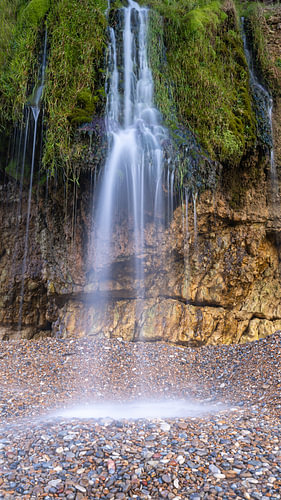 Kustlandschap van Normandië met waterval vanaf de krijtrotsen en drooggevallen strand