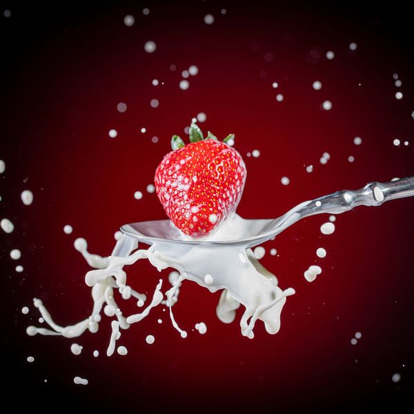 A delicious, ripe, red strawberry falls onto a tablespoon of milk by Photo Art Thomas Klee