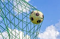 Football shot in goal net with blue sky