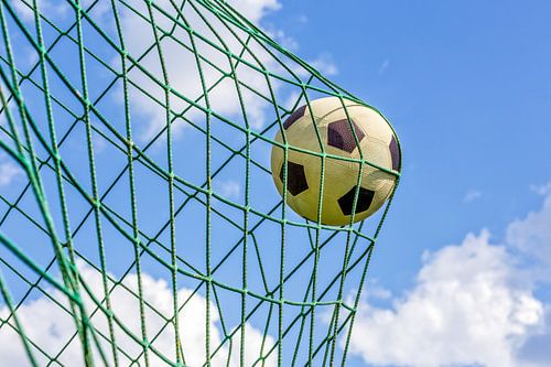 Football shot in goal net with blue sky