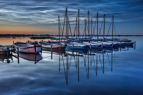 Een landchap van lichtende nachtwolken, noctilucent clouds, die refelcteren, of weerepigelen in het water van het meer, zeilboten liggen stil aan de steiger
