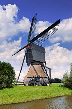 Dutch ancient wooden windmill near small canal on a sunny day  by Tony Vingerhoets