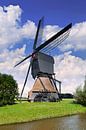 Dutch ancient wooden windmill near small canal on a sunny day  by Tony Vingerhoets thumbnail