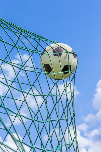 Football caught in goal net with blue sky