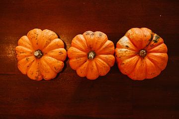 drie oranje pompoenen op een rij op tafel van Margriet Hulsker