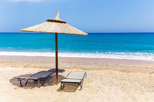 Rieten parasol met ligstoelen aan strand op grieks eiland Kefalonia
