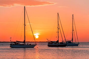 Oranje zonsondergang met zeilboten aan de kust op zee van Ben Schonewille
