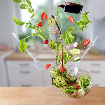 Vliegende salade, sla, tomaten, komkommers en radijs vallen met olie en azijn in een kom in de keuke van Maren Winter