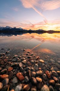 Spiegelung mit Ufersteinen des Sonnenuntergangs am Hopfensee im Allgäu