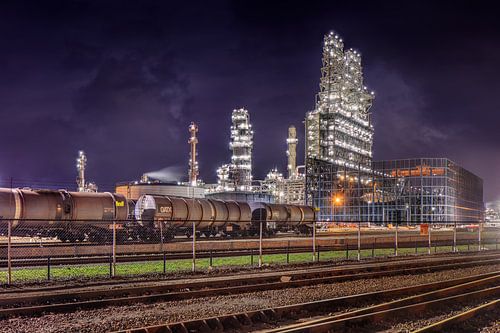 Row of train wagons with oil refinery against a purple sky