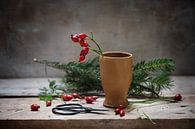 het voorbereiden van natuurlijke kerstversiering met rozenbottels in een aardewerken vaas en dennent van Maren Winter thumbnail
