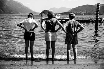 Schwarz-Weiß-Fotografie von drei Frauen mit Händen an den Seiten, die auf einen See in Italien blick von Monique Tekstra-van Lochem
