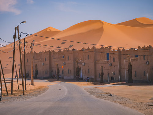 Sanddünen, die eine Kasbah in Merzouga überragen