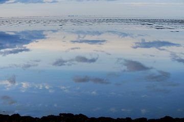 Wolken weerspiegelen in het water van de Waddenzee.