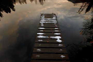 Met sneeuw en gebladerte bedekte houten voetgangersbrug over door wolken weerkaatst wateroppervlak van Besa Art