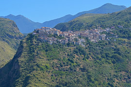 Hill town perched on green mountain landscape under blue sky by Tomherkules