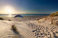 man paragliding op strand bij zonsondergang over zee in de zomer