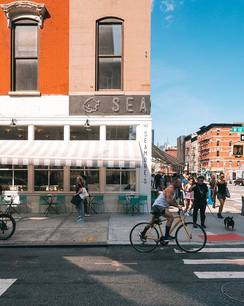 Straßenecke mit orangefarbenem Gebäude, Restaurant und Radfahrer in Manhattan, New York von Michiel Dros