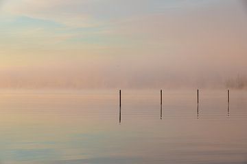 misty sunrise over the water with reflective poles and pastel colors by Kim Willems