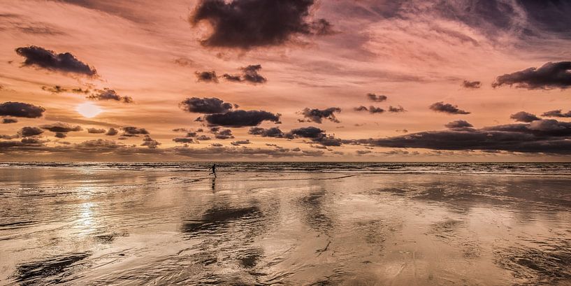 Hardloper op het strand bij eb in het gekleurde avondlicht van Harrie Muis