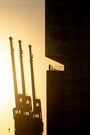 Backlighting in the harbour: a figure and the silhouette of a crane in front of the Elbphilharmonie by Nils Steiner