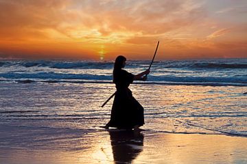 Jeune femme samouraï avec un sabre japonais (Katana) au coucher du soleil sur la plage sur Eye on You
