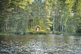 Rood houten huis aan een Zweeds meer met een weerspiegeling van het bos in een natuurlijke omgeving.